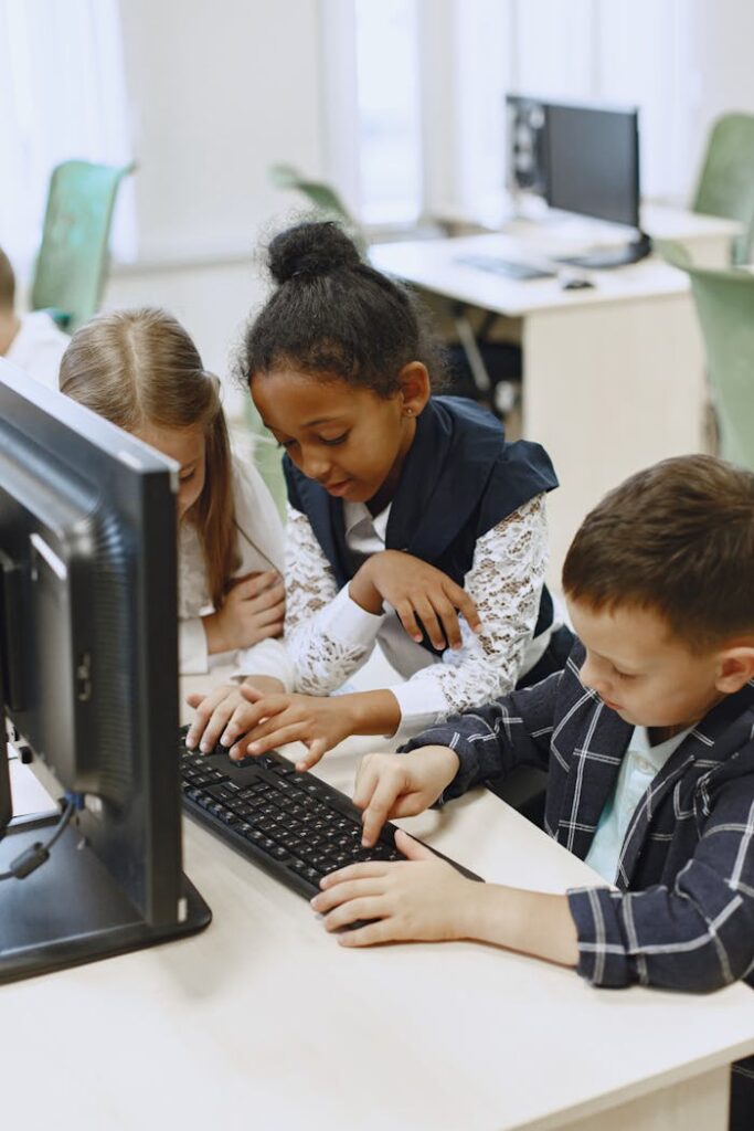 Three children work together on a computer in a school lab, learning and collaborating.